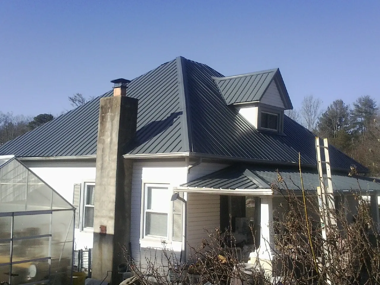 Dark blue standing seam metal roof on a white farmhouse with dormer — Slate & Tile Roof Repair by Roofing Brothers in New Canaan