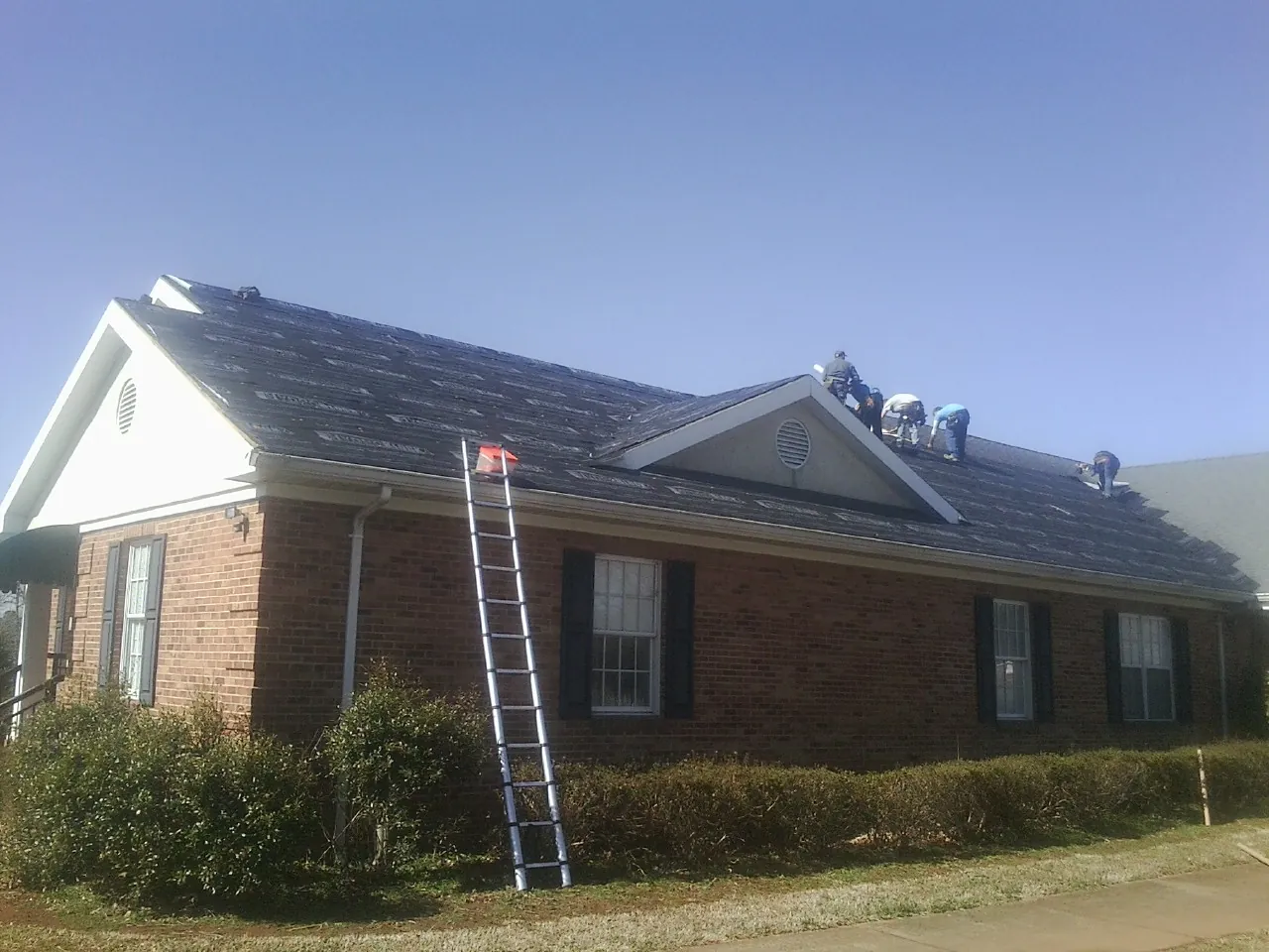 Crew tearing shingles off a brick ranch roof with a ladder set — Metal Roof Repair work by our crew in New Canaan