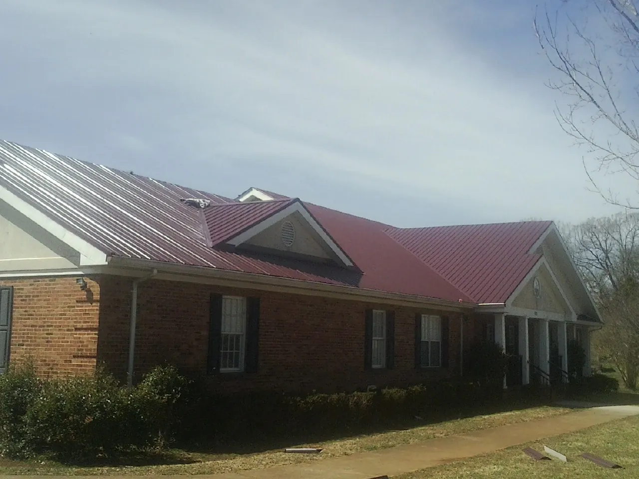 Red metal roof with gabled entries on a long brick building, from a Hail Damage Roof Repair job in New Canaan