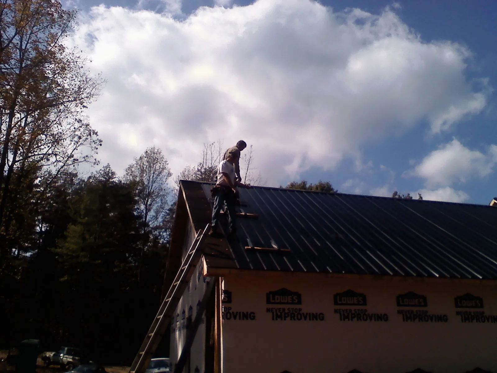 Roofer fastening dark metal panels high against a cloudy sky, from a Roof Inspection job in New Canaan