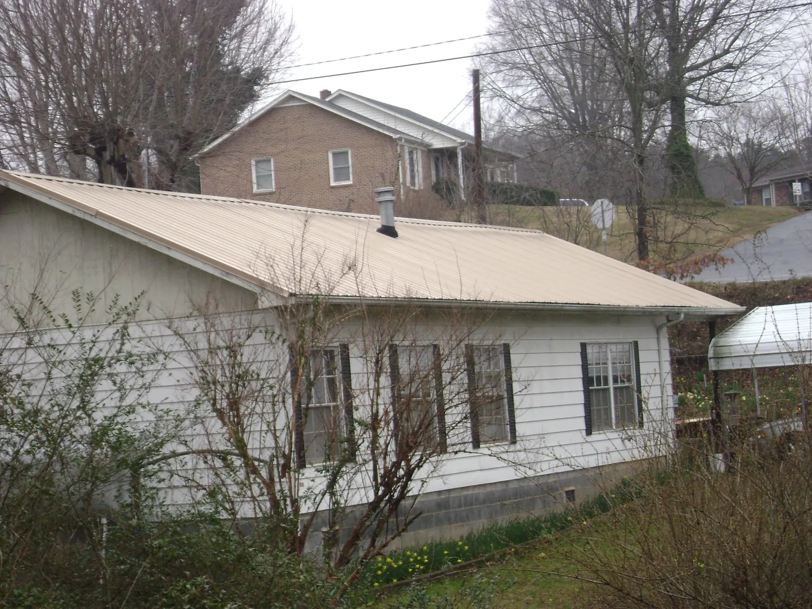 Tan metal roof on a white sided house set into a hillside — Commercial Roofing by Roofing Brothers in New Canaan