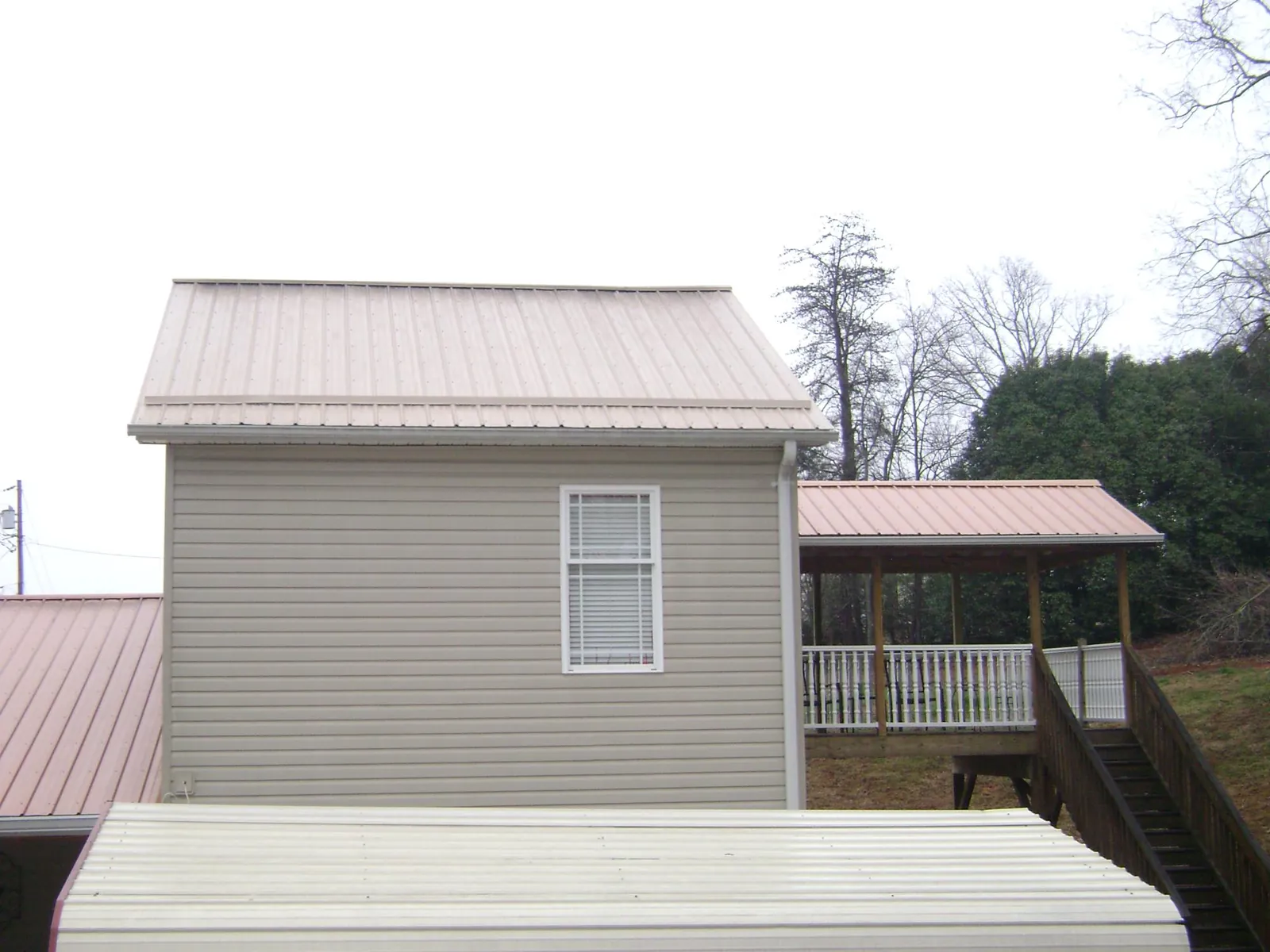 Tan metal roofs on a two story addition and attached porch, from a Roof Replacement job in New Canaan